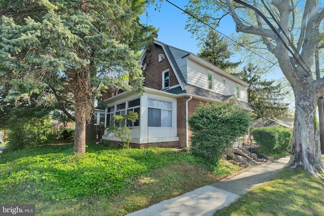 view of side of home featuring brick siding, a shingled roof, and a sunroom