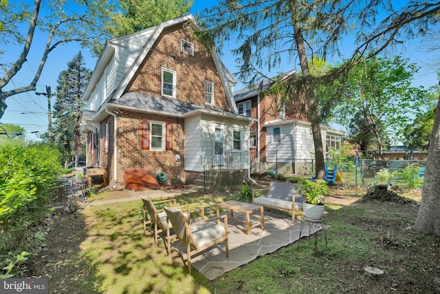 rear view of property with fence, a patio area, a gambrel roof, and brick siding