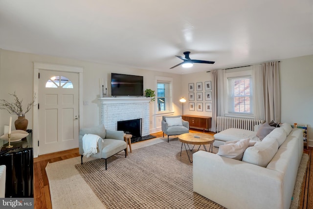 living room with a healthy amount of sunlight, radiator, a ceiling fan, and a brick fireplace