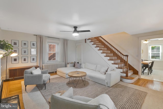 living room with wood finished floors, a ceiling fan, radiator, and stairs