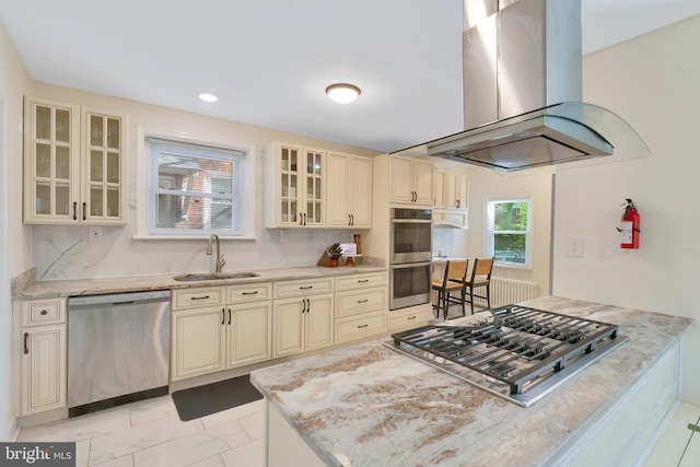 kitchen with marble finish floor, island range hood, cream cabinets, a sink, and appliances with stainless steel finishes