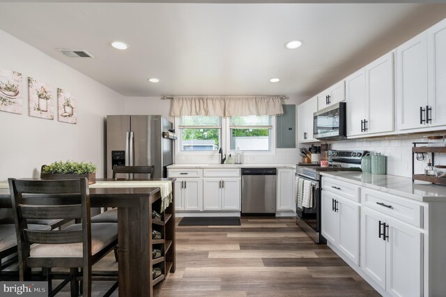 kitchen with white cabinets, stainless steel appliances, wood finished floors, and visible vents