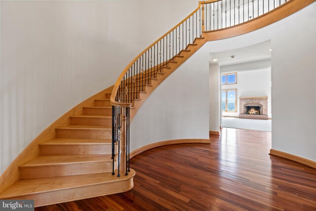 staircase featuring a towering ceiling, wood-type flooring, baseboards, and a fireplace
