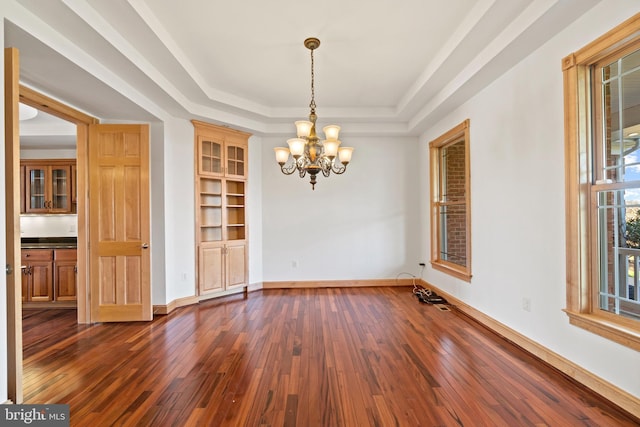 unfurnished dining area with a chandelier, dark wood finished floors, a tray ceiling, and baseboards