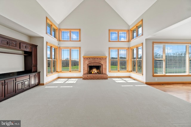 unfurnished living room featuring baseboards, a brick fireplace, high vaulted ceiling, and carpet
