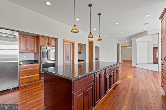 kitchen with stainless steel appliances, dark countertops, wood-type flooring, a kitchen island, and hanging light fixtures