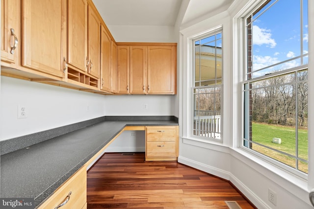 unfurnished office featuring built in desk, healthy amount of natural light, and dark wood-style floors