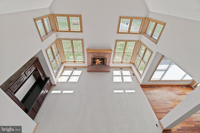 unfurnished living room featuring a high ceiling, plenty of natural light, a brick fireplace, wood finished floors, and baseboards