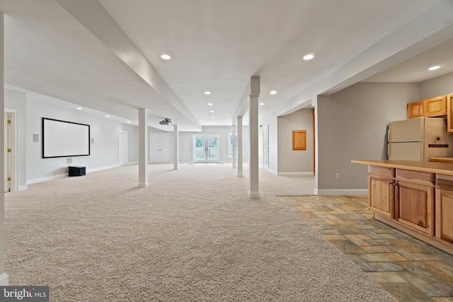below grade area featuring freestanding refrigerator, baseboards, stone tile floors, recessed lighting, and light carpet