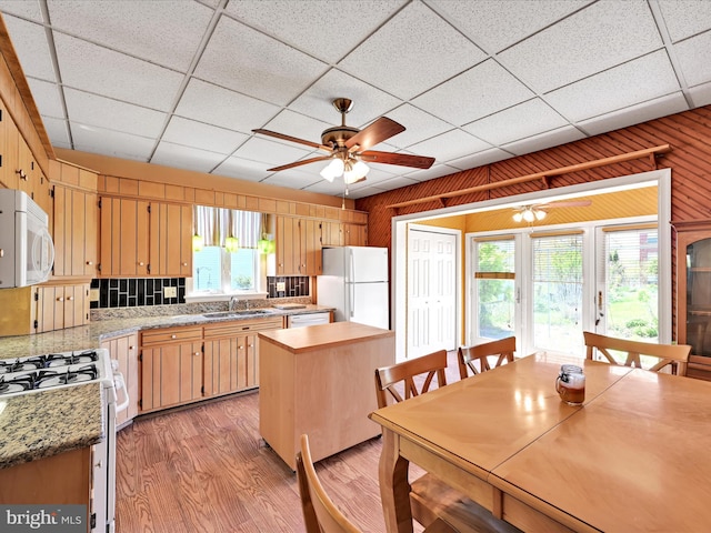 kitchen with wooden walls, ceiling fan, a sink, white appliances, and light wood-type flooring