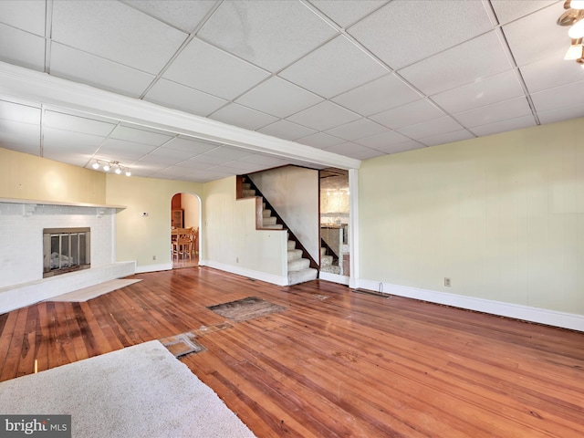 unfurnished living room with a brick fireplace, arched walkways, hardwood / wood-style floors, stairs, and baseboards