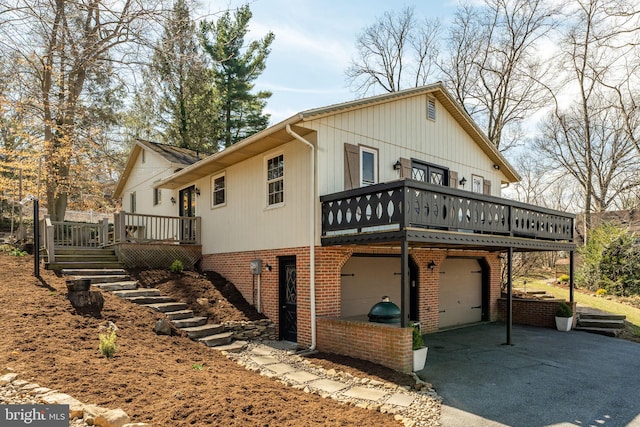 view of side of property featuring driveway, a wooden deck, brick siding, an attached garage, and stairs
