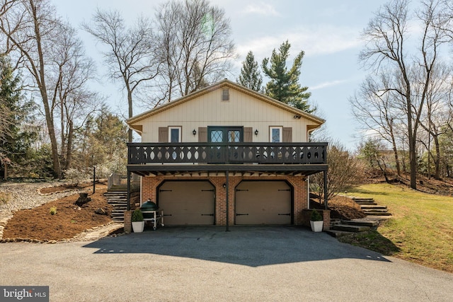 view of front of house featuring a garage, aphalt driveway, a deck, stairs, and brick siding