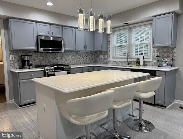 kitchen with gray cabinets, a sink, light countertops, a breakfast bar, and stainless steel appliances