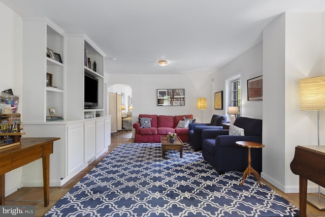 tiled living area with baseboards, arched walkways, and built in features