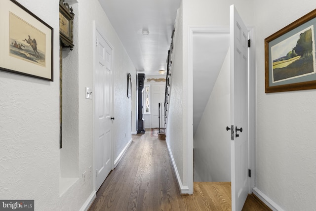 corridor featuring baseboards, a textured wall, and wood finished floors
