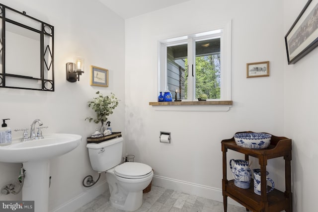 half bathroom featuring baseboards, a sink, and toilet