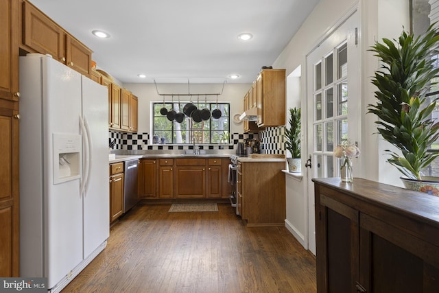 kitchen with tasteful backsplash, dishwasher, light countertops, white fridge with ice dispenser, and dark wood-type flooring