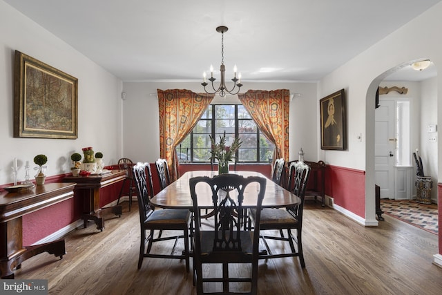 dining room with arched walkways, baseboards, an inviting chandelier, and wood finished floors