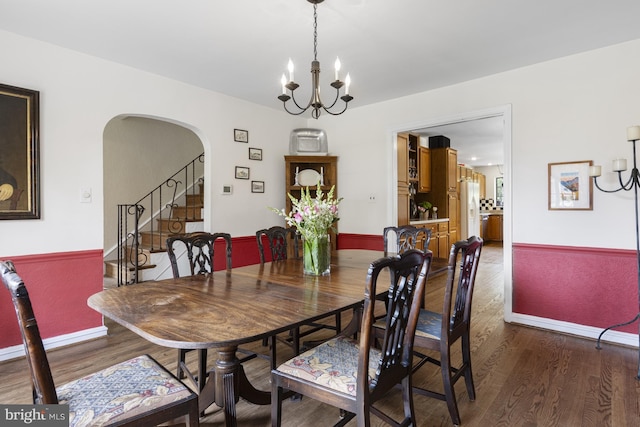 dining space with baseboards, arched walkways, wood finished floors, and a notable chandelier