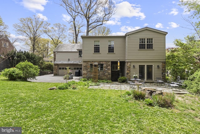 rear view of house with a lawn, an attached garage, a patio area, and stone siding