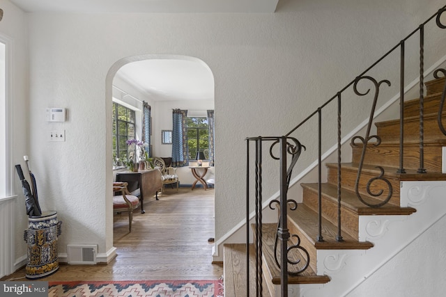 entrance foyer featuring arched walkways, a textured wall, stairs, and wood finished floors