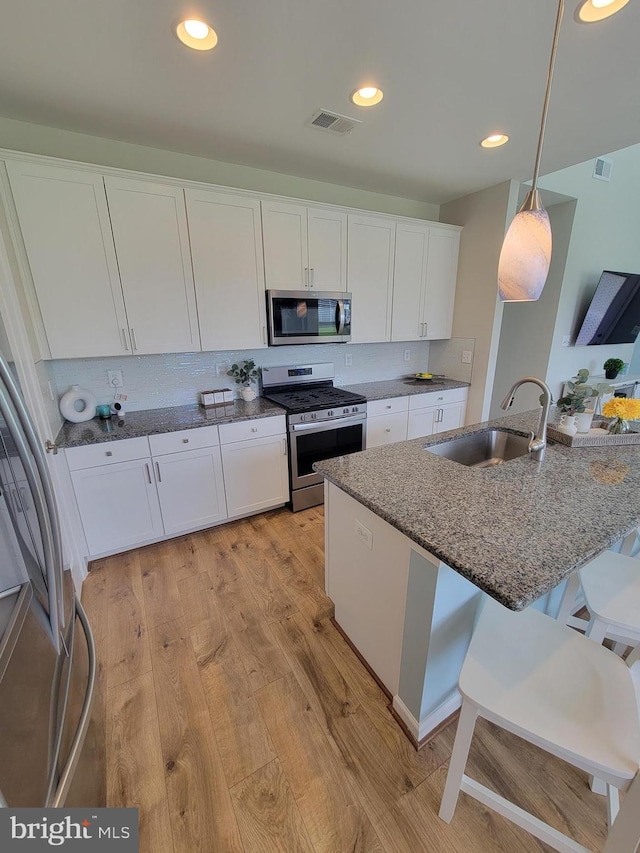kitchen with visible vents, white cabinets, a sink, light wood finished floors, and appliances with stainless steel finishes