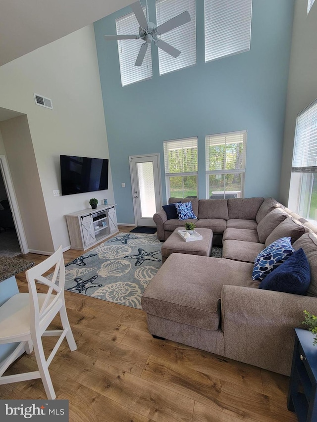 living area featuring visible vents, a towering ceiling, wood finished floors, and ceiling fan
