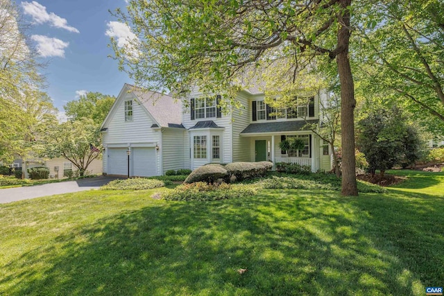 traditional home featuring roof with shingles, an attached garage, a front yard, and aphalt driveway