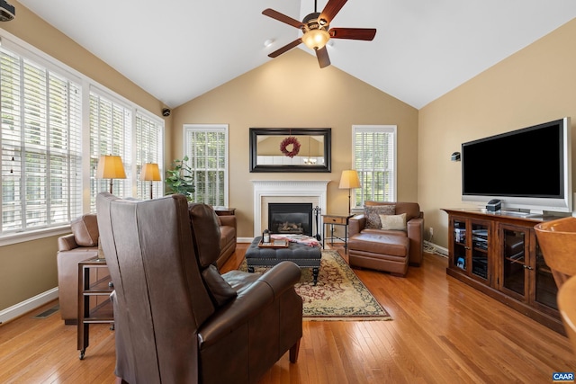 living area with ceiling fan, a glass covered fireplace, plenty of natural light, and light wood-style floors