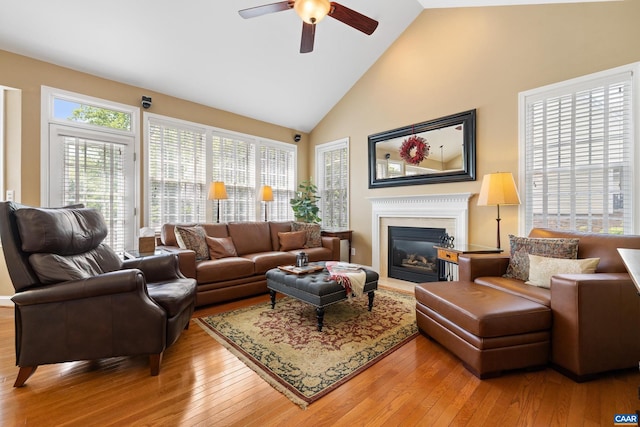 living room with a glass covered fireplace, high vaulted ceiling, ceiling fan, and light wood finished floors