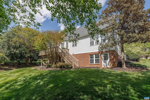 rear view of house featuring stairs, a shingled roof, brick siding, a wooden deck, and a lawn