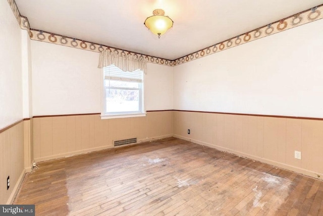 unfurnished room featuring wood-type flooring, visible vents, and wainscoting