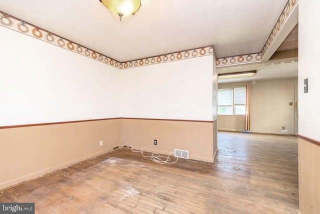 empty room featuring a wainscoted wall, wood finished floors, and visible vents