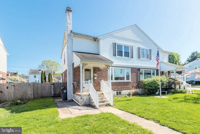 view of front facade with fence, a chimney, a front yard, and brick siding