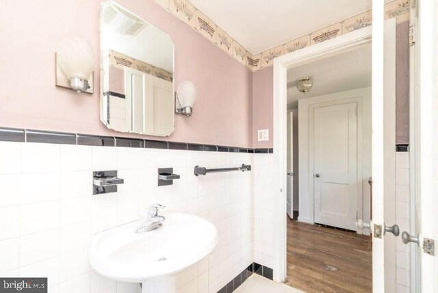 bathroom with visible vents, wood finished floors, tile walls, a wainscoted wall, and a sink