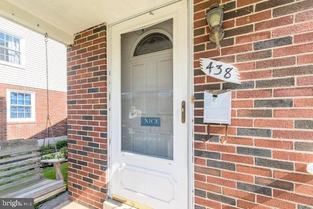 doorway to property with a porch and brick siding