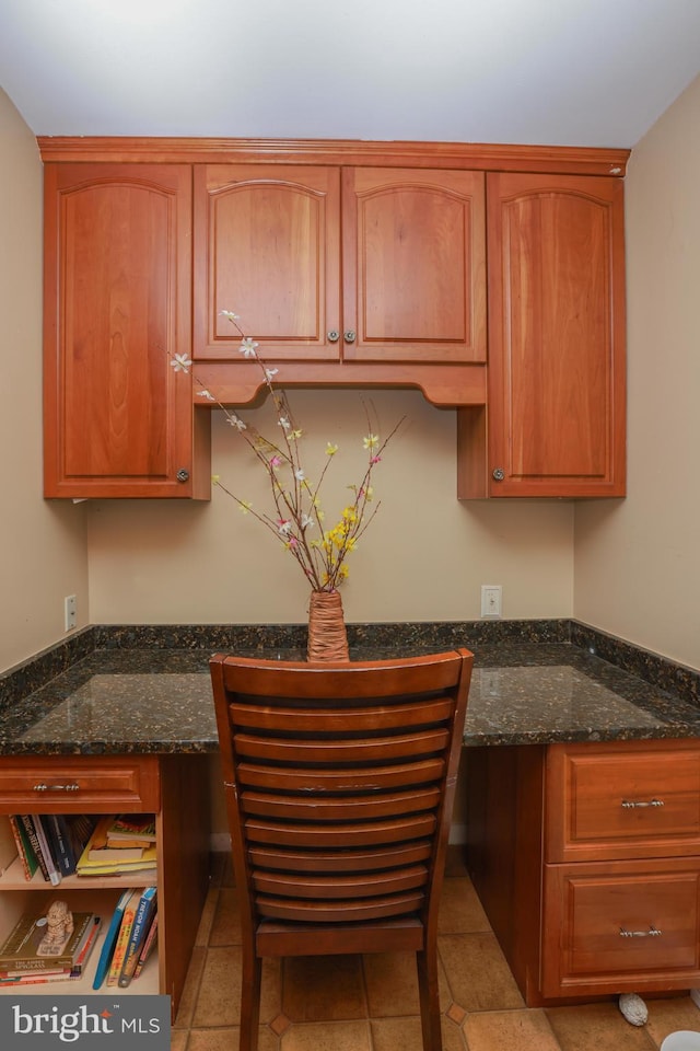 kitchen featuring brown cabinets, dark stone countertops, and built in desk