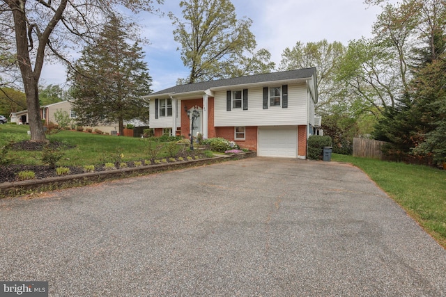 bi-level home featuring driveway, a garage, brick siding, fence, and a front lawn