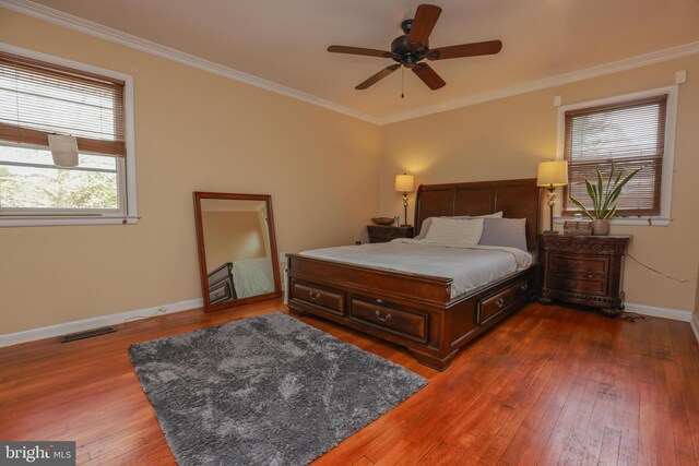 bedroom featuring ceiling fan, visible vents, crown molding, baseboards, and wood-type flooring