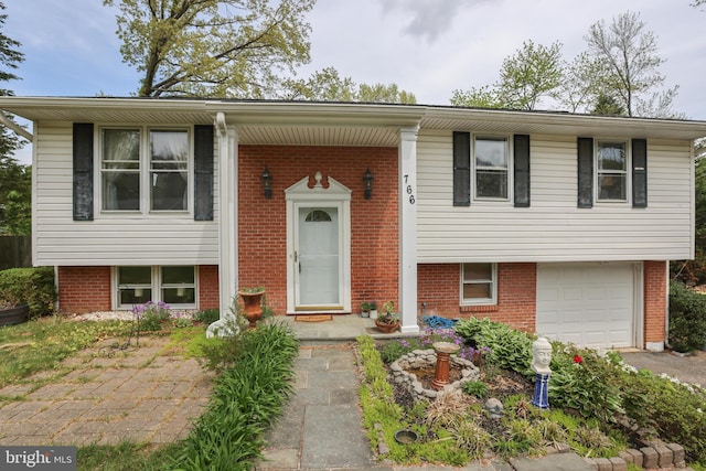 split foyer home featuring a garage, driveway, and brick siding