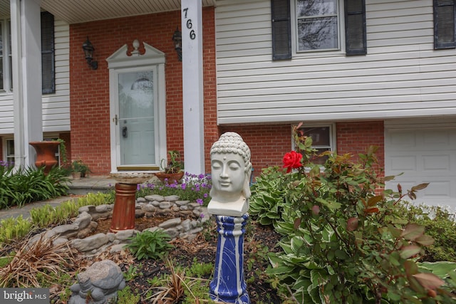 doorway to property with brick siding, a garage, and covered porch