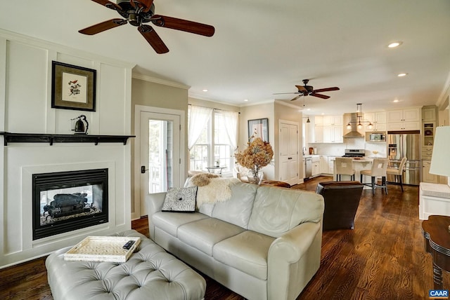 living area with a glass covered fireplace, ceiling fan, ornamental molding, and recessed lighting