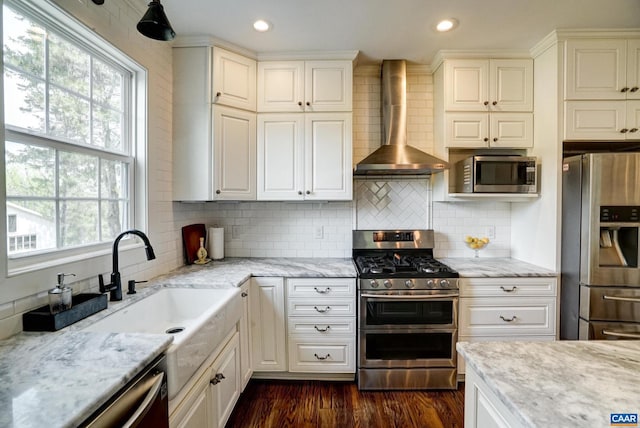 kitchen featuring wall chimney range hood, appliances with stainless steel finishes, light stone countertops, and backsplash