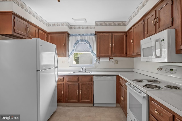 kitchen with a sink, brown cabinets, white appliances, and light countertops