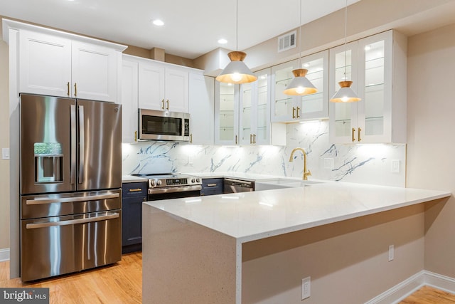 kitchen with glass insert cabinets, light wood-type flooring, light stone counters, a sink, and appliances with stainless steel finishes