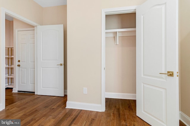 unfurnished bedroom featuring baseboards, wood finished floors, and a closet