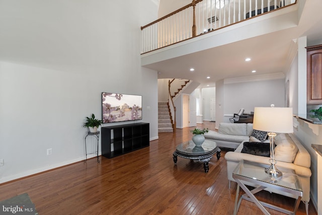 living room with hardwood / wood-style flooring, baseboards, ornamental molding, a high ceiling, and stairs