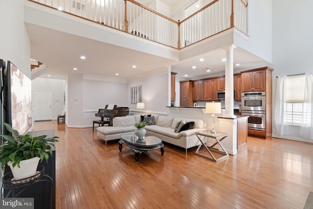 living area with visible vents, light wood-type flooring, ornate columns, and a towering ceiling