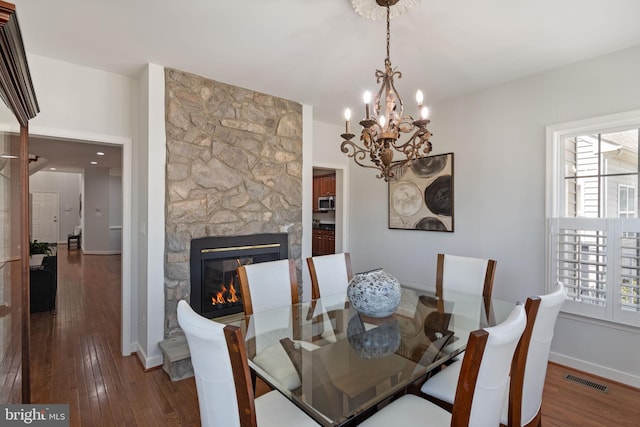 dining area with a notable chandelier, a stone fireplace, baseboards, visible vents, and hardwood / wood-style flooring